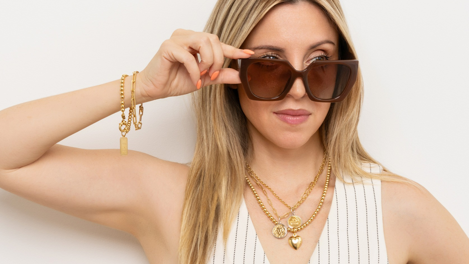 Woman wearing sunglasses and gold jewelry against a white background