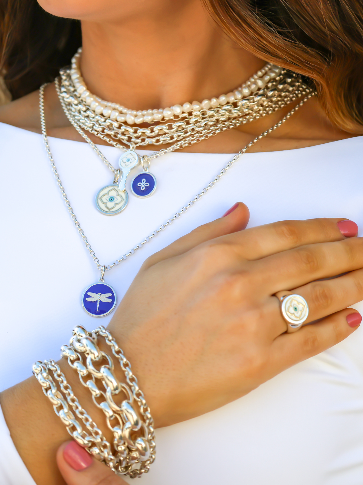 Close-up of a person wearing multiple necklaces, bracelets, and a ring on a white background