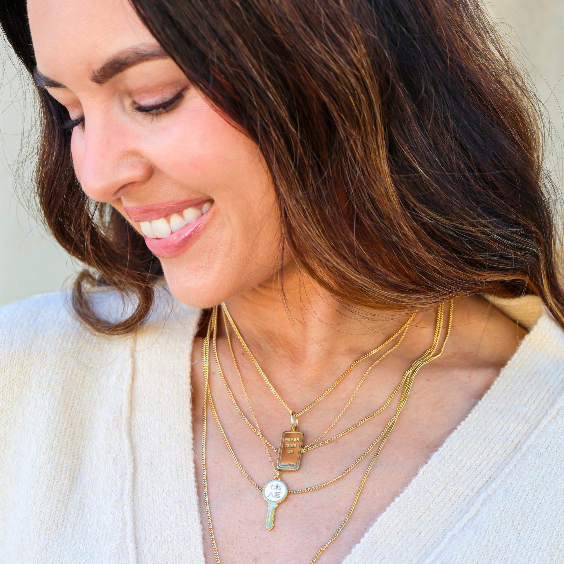 Woman wearing multiple gold necklaces with pendants, smiling outdoors. - 2