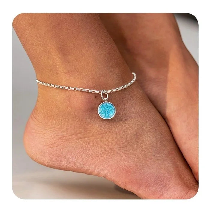 Silver anklet with a blue charm on a foot against a neutral background